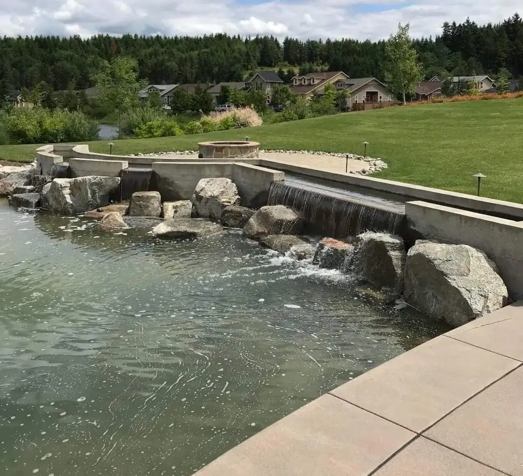 Wide view of the multi-level concrete water feature and surrounding patio in Puyallup, WA, with a fire pit.