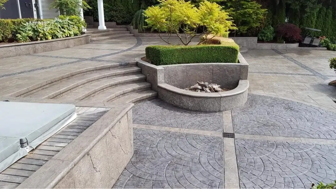 Wide view of a multi-level stamped concrete patio in Burien, WA with curved steps and an integrated planter.