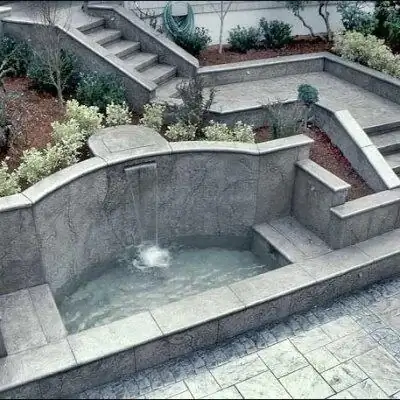 A custom stamped concrete water feature with a small waterfall, integrated into a retaining wall.