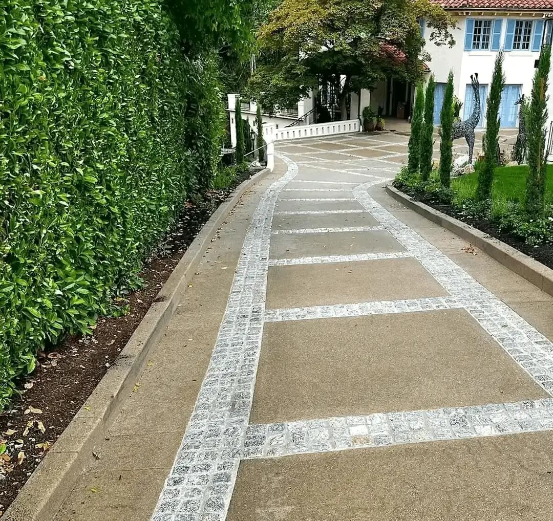 Finished exposed aggregate concrete driveway in Seattle with a curving path and inlaid cobblestone grid pattern.
