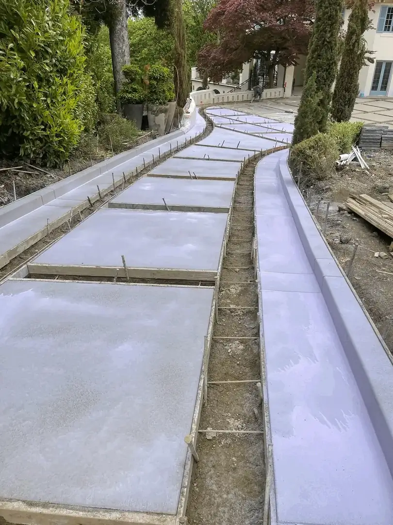 Freshly poured concrete sections curing within wooden forms for a long, curving residential driveway.