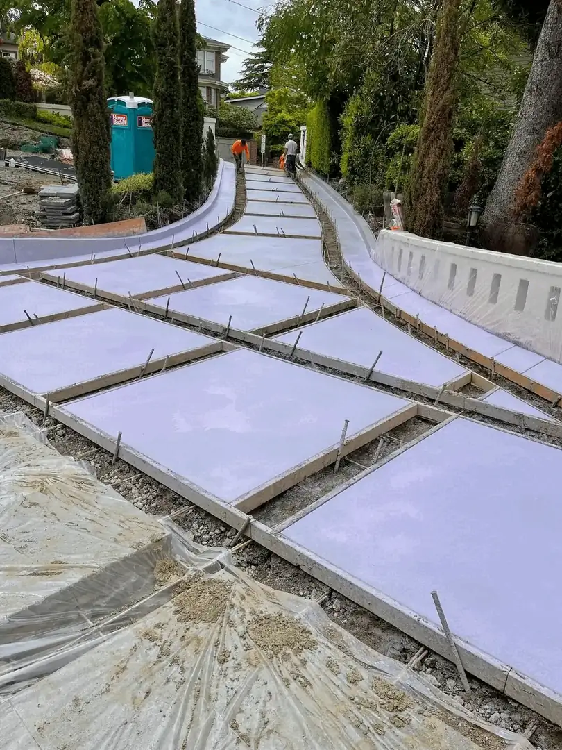 Workers finishing the surface of freshly poured concrete driveway sections with a slight curve.