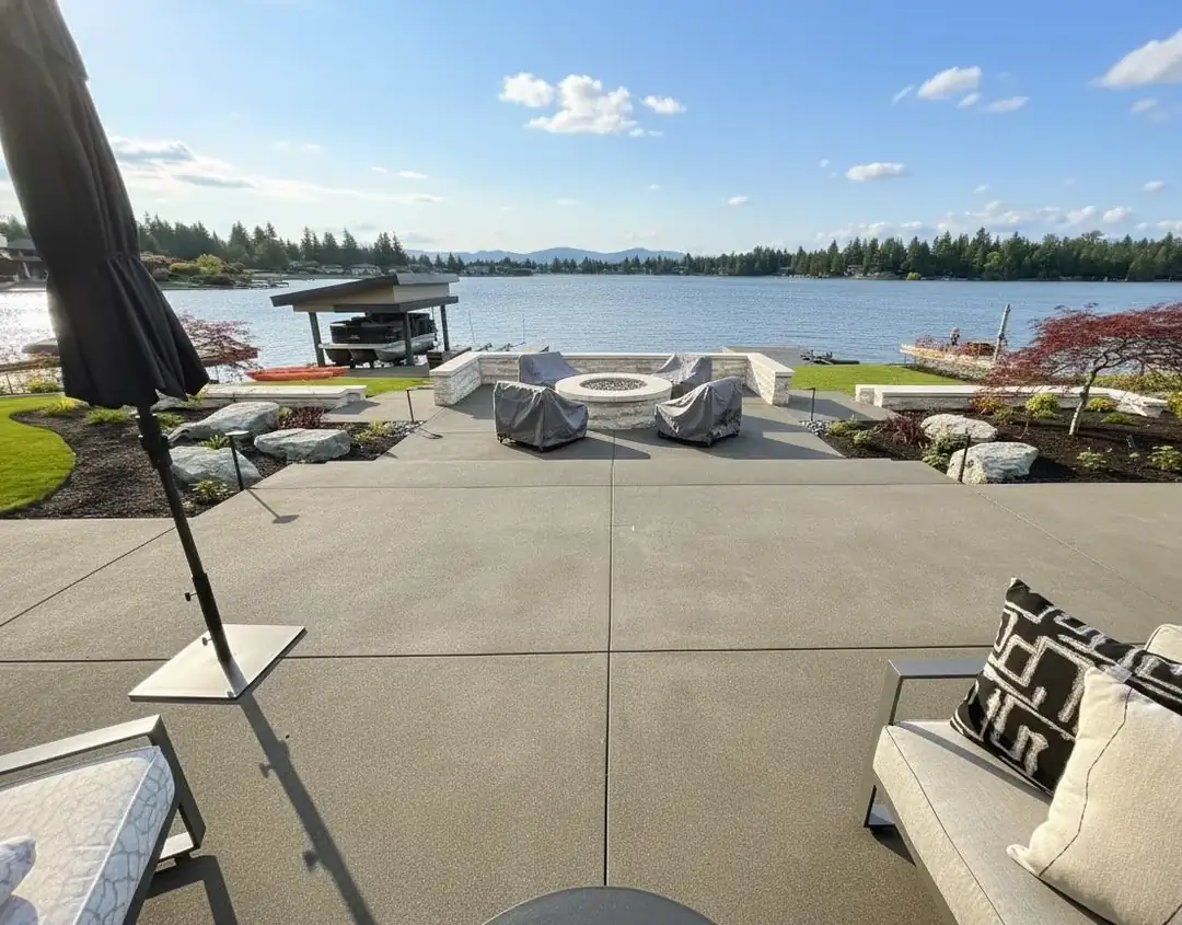 Lakeside exposed aggregate concrete patio with a fire pit and seating area in Puyallup, WA, overlooking the water.