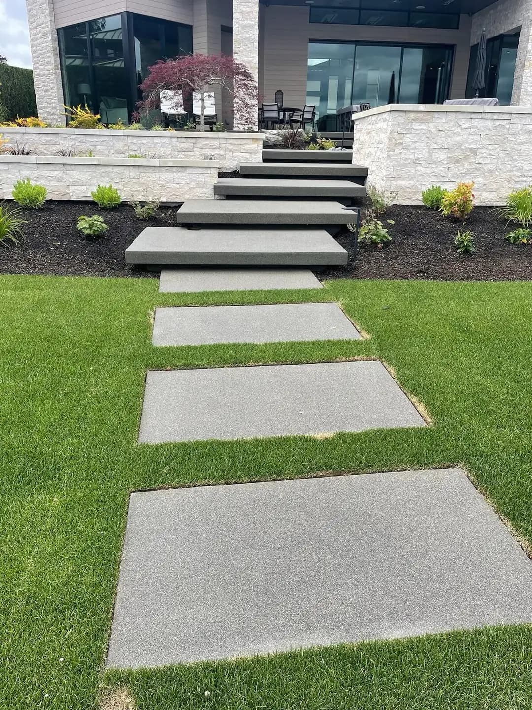 A series of rectangular exposed aggregate stepping stones forming a walkway across a manicured green lawn.