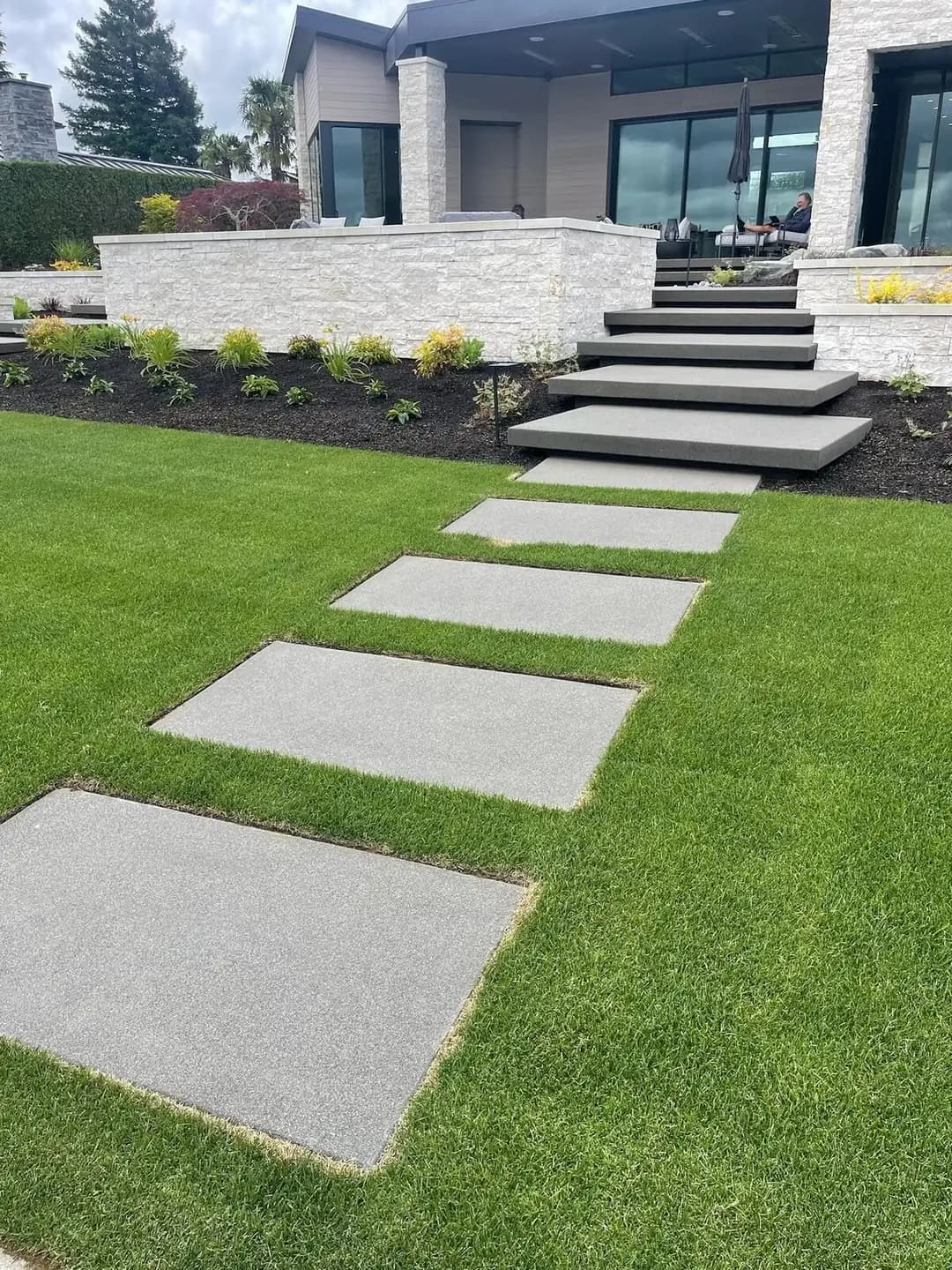Angled perspective of a concrete slab walkway transitioning into a set of floating steps up to the house.