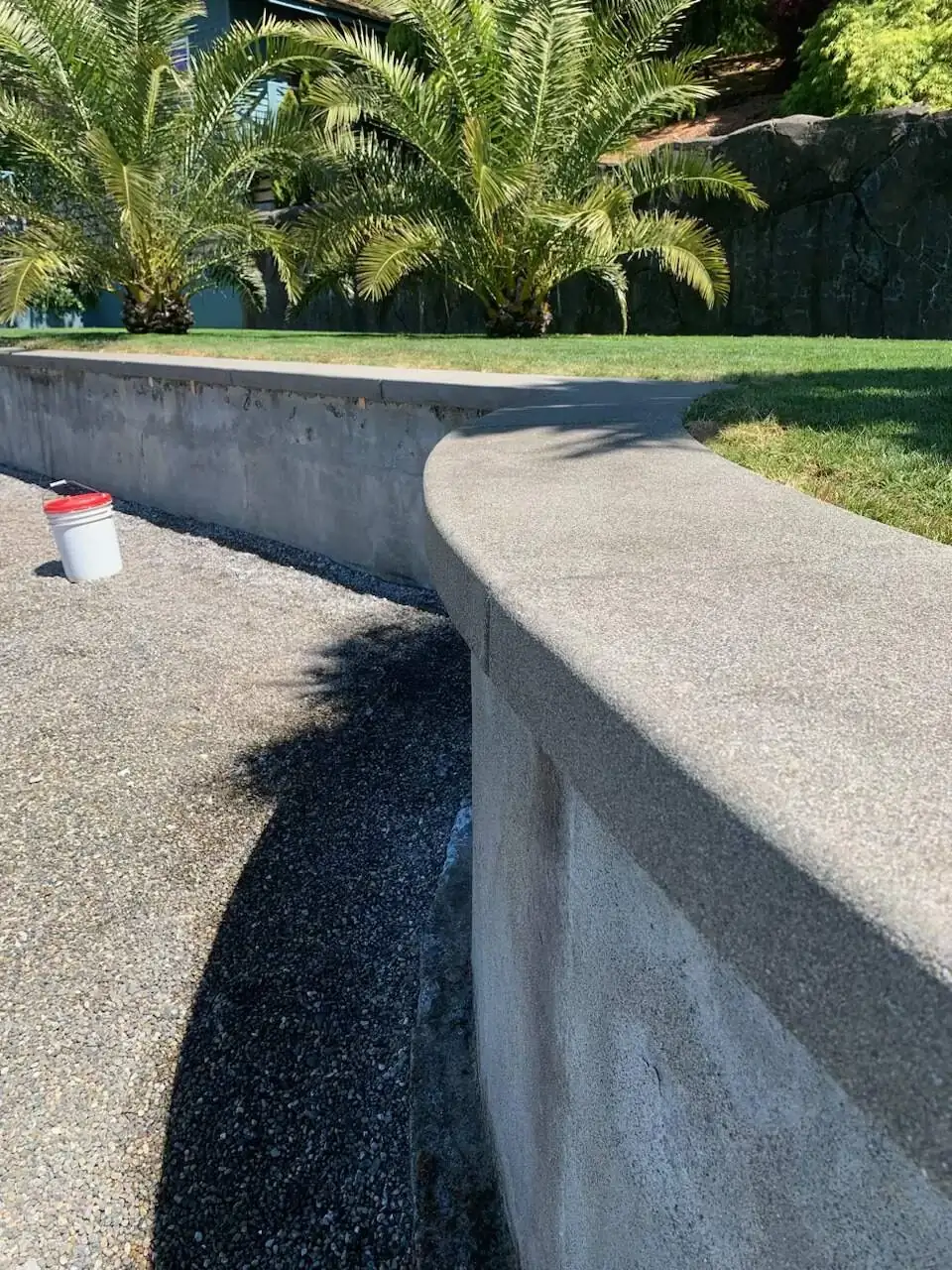 View along the top of a curved sand finish concrete retaining wall with a rounded cap in Puyallup, WA.