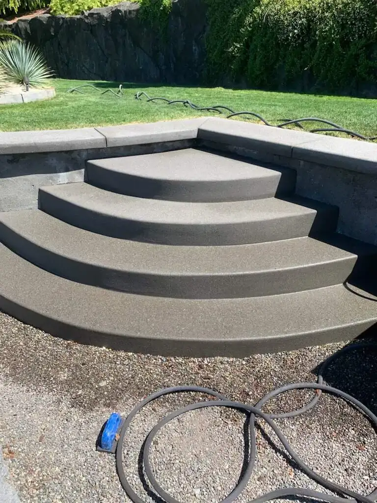 A set of wide, curved concrete steps with a dark sand finish connecting two landscape tiers.