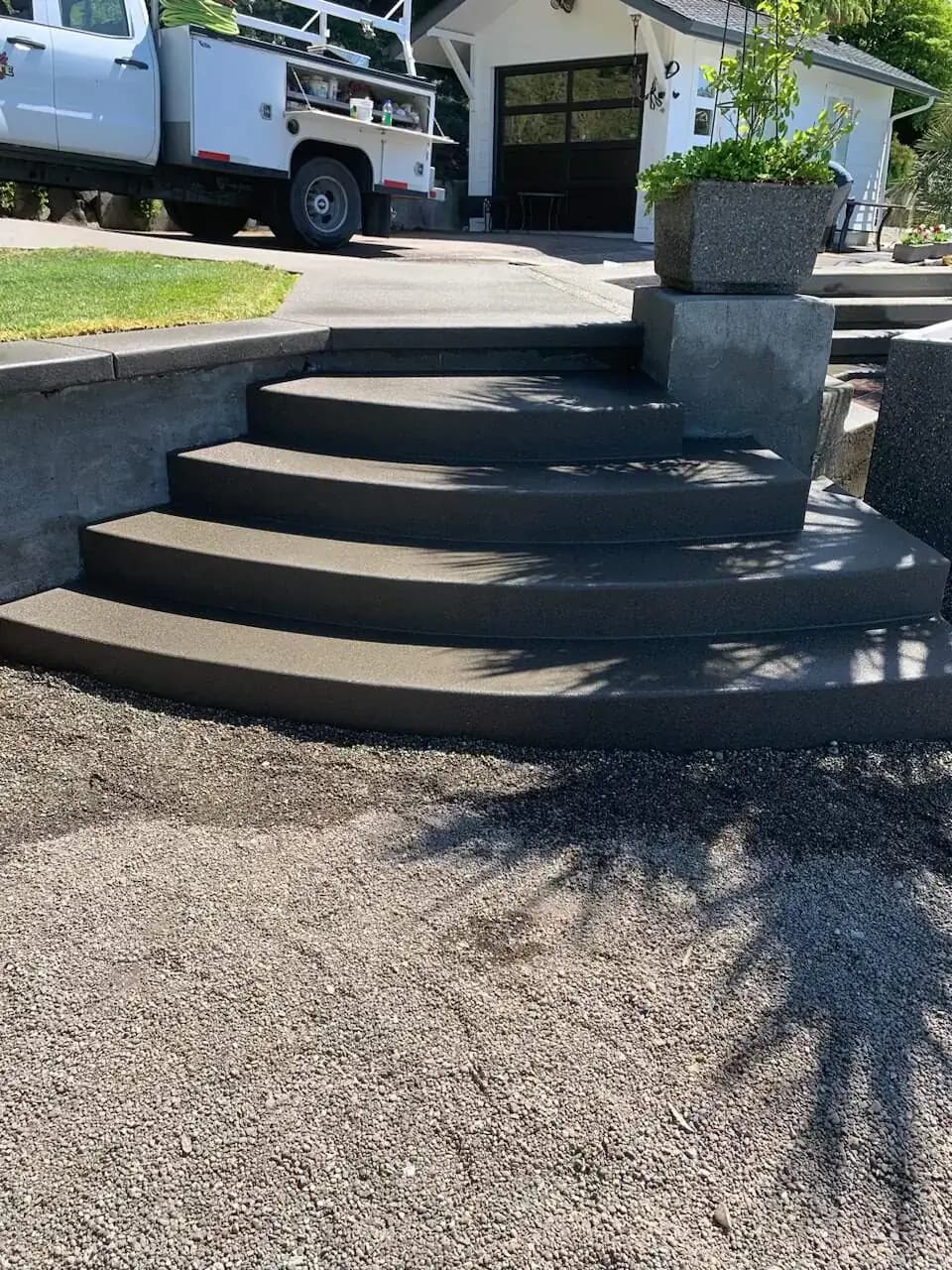 Full view of the multi-tiered curved concrete steps leading up from a gravel path to a driveway.