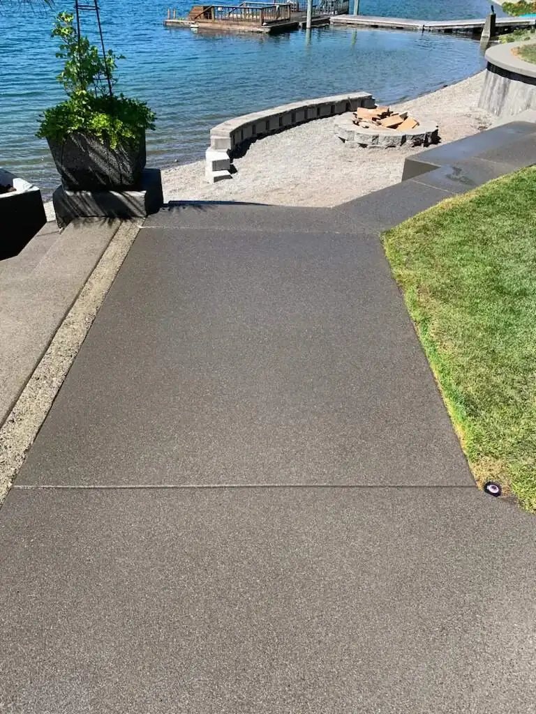 A sand finish concrete walkway leading down towards a waterfront fire pit and seating area.