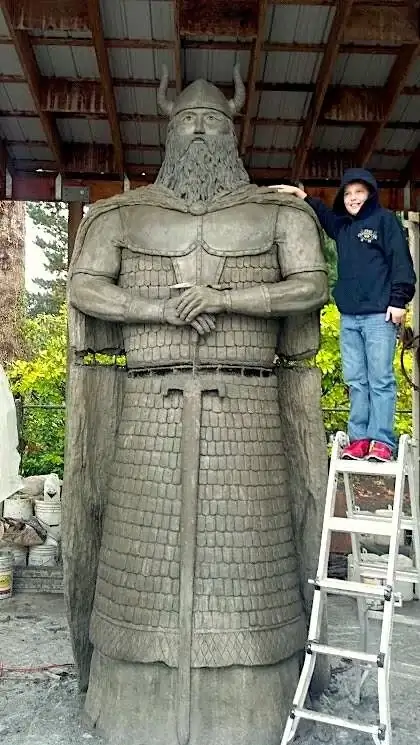 Full view of the large-scale custom concrete warrior statue in Puyallup, with a person for scale comparison.
