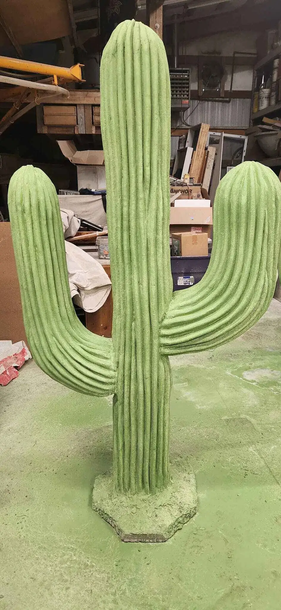 A front view of an unfinished concrete cactus inside a fabrication shop, highlighting its form.