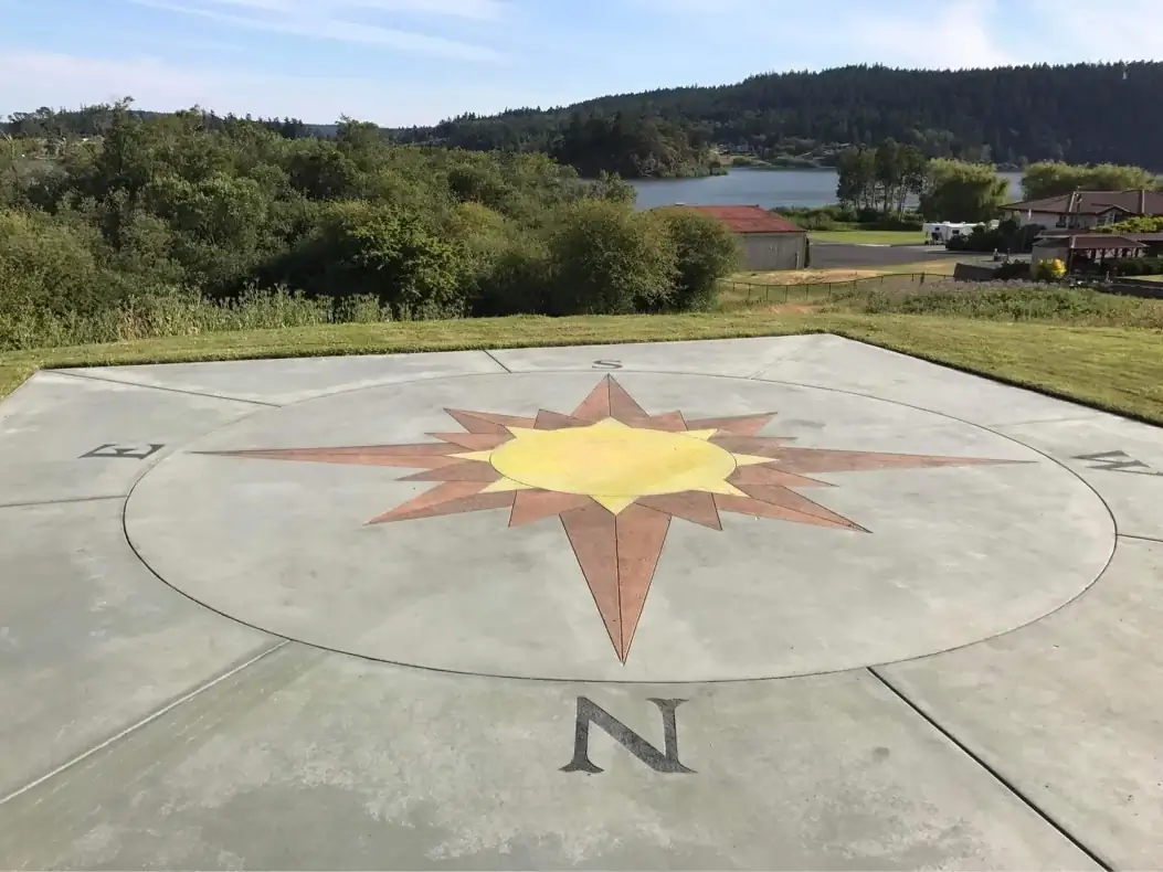 A ground-level perspective of the custom concrete compass rose with a scenic lake view in the background.