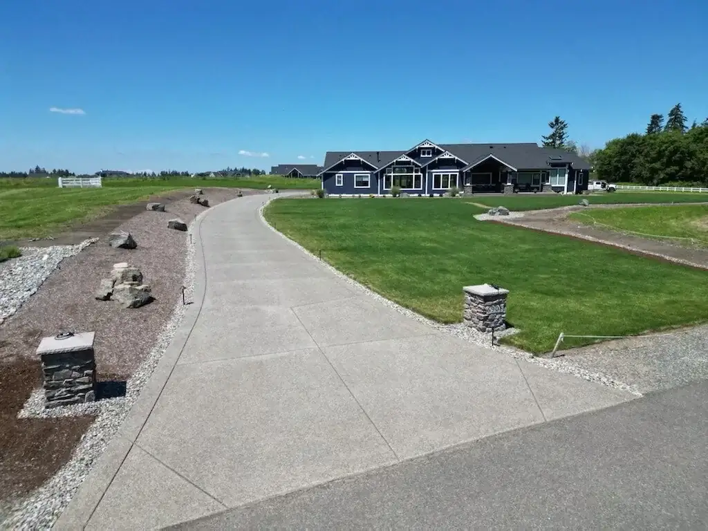 Finished exposed aggregate concrete driveway in Buckley, WA with saw-cut control joints curving through a large lawn.