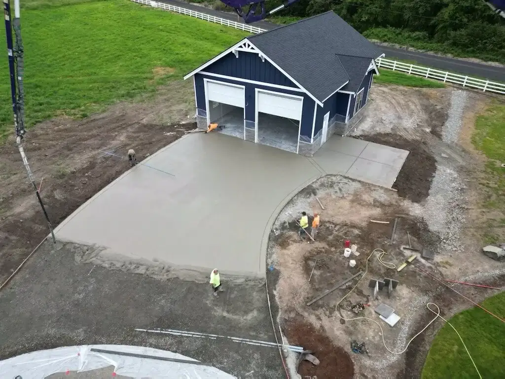Workers finishing a freshly poured concrete driveway and garage apron for a new construction project in Buckley, WA.