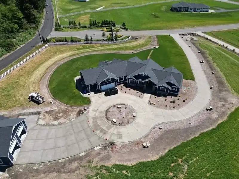 Overhead drone shot of a complete exposed aggregate driveway system with a circular turnaround and long approach.