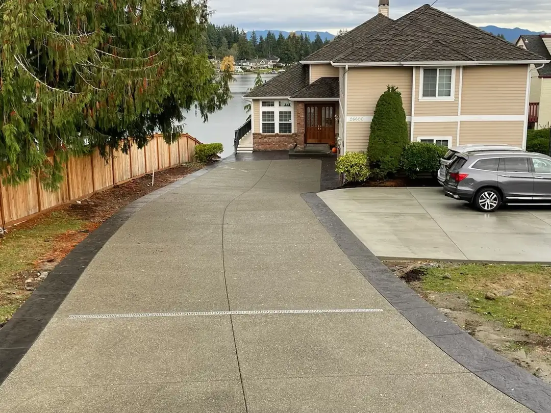 High-angle view of a long, curving exposed aggregate concrete driveway with a dark stamped border in Kent, WA.
