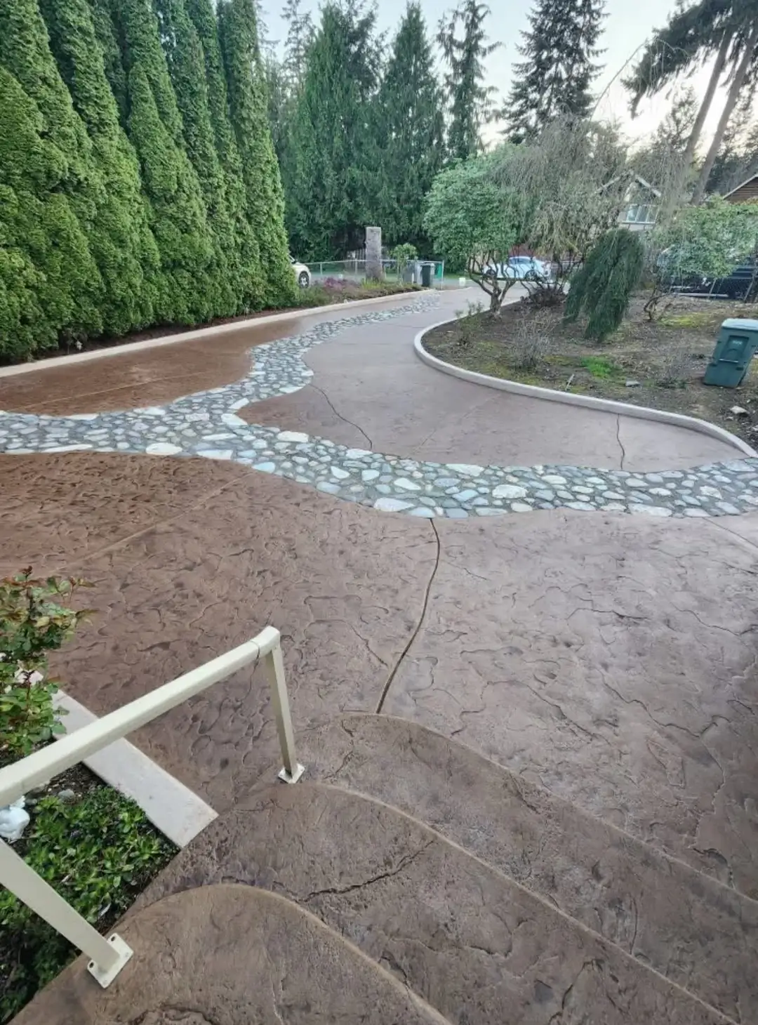 View from the top of stamped concrete steps in Puyallup, looking down the long, winding driveway with stone inlay.