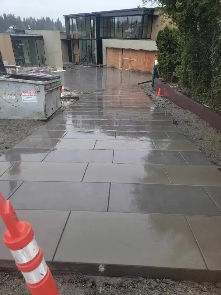 Perspective shot looking up a modern concrete driveway towards a contemporary house with large glass windows.