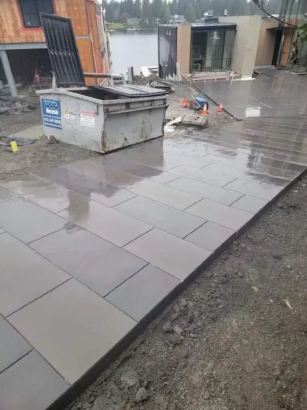 A newly finished concrete patio and walkway with a reflective, wet surface next to a modern building.