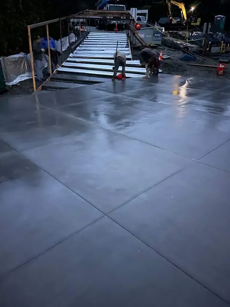 Workers troweling a large expanse of fresh concrete at night, creating a smooth, uniform surface.