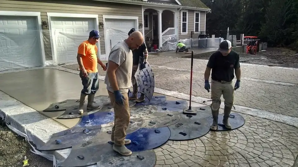 Craftsmen applying a European fan stamp pattern to freshly poured concrete for a new driveway in Bellevue.