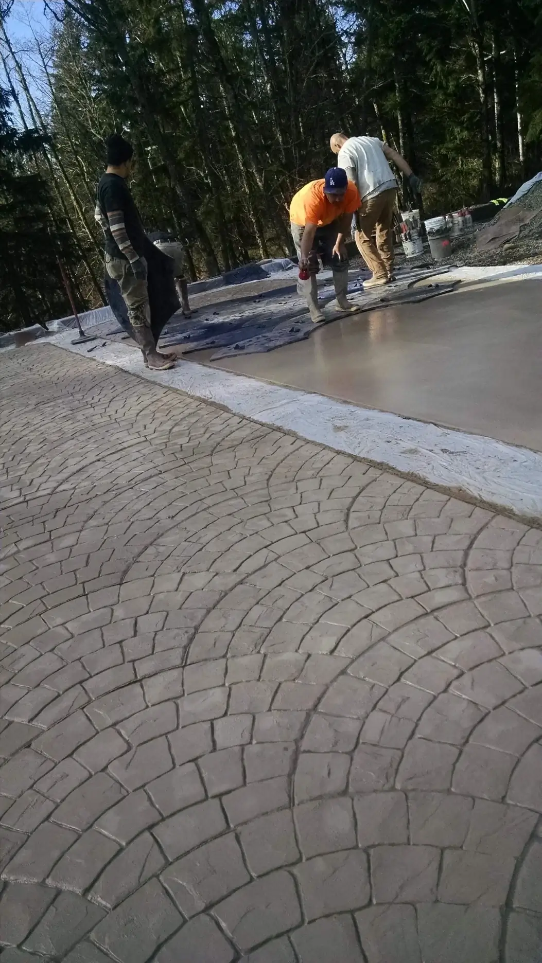 A crew works on the edge of a large concrete pour, preparing the surface for the stamping application.