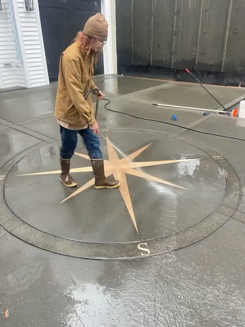 A craftsman pressure washing the newly installed decorative concrete driveway in Bellevue to reveal the final colors.
