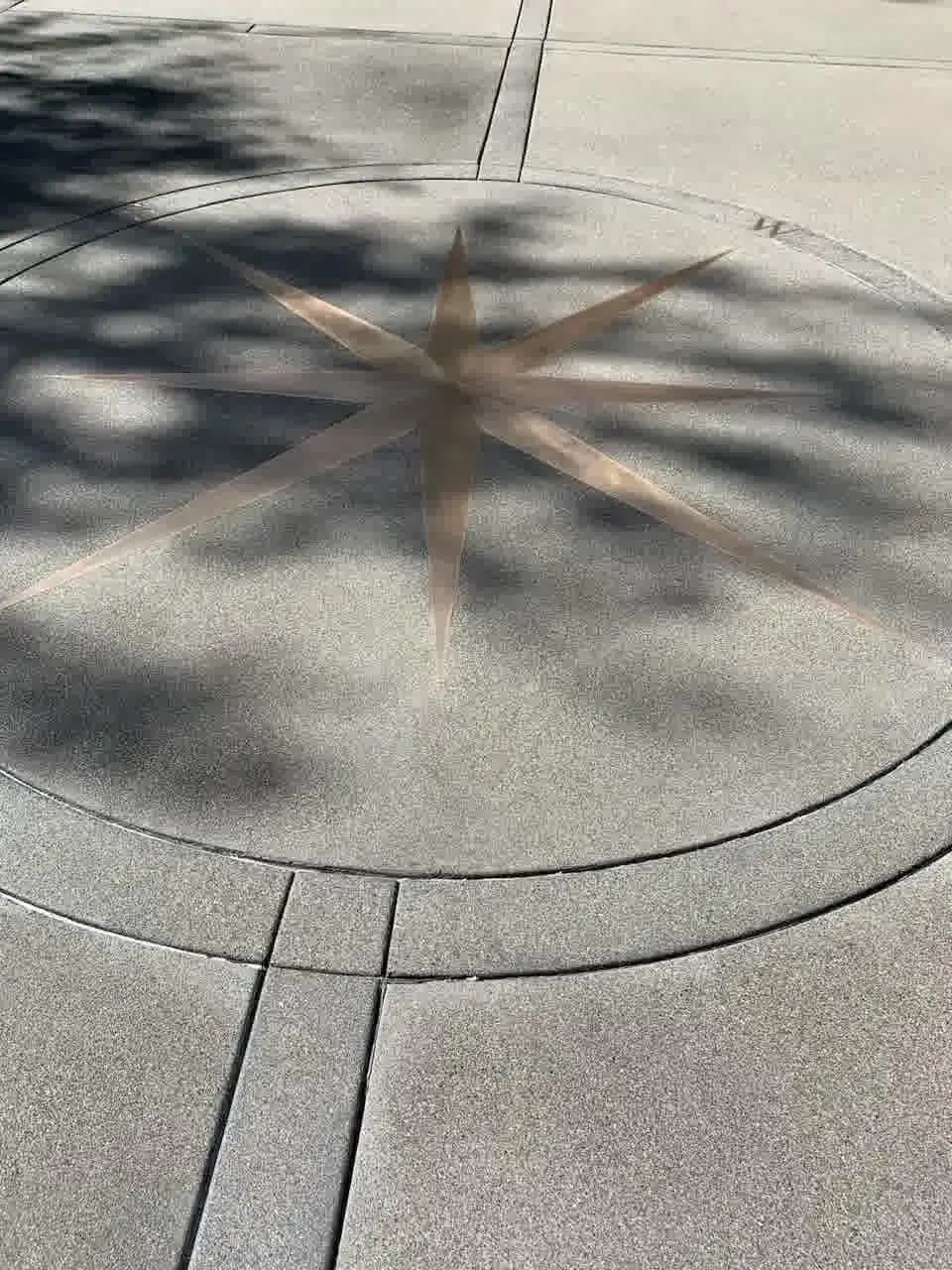 A dry view of the sand finish concrete driveway in Bellevue, showing the saw-cut joints and the subtle compass design.