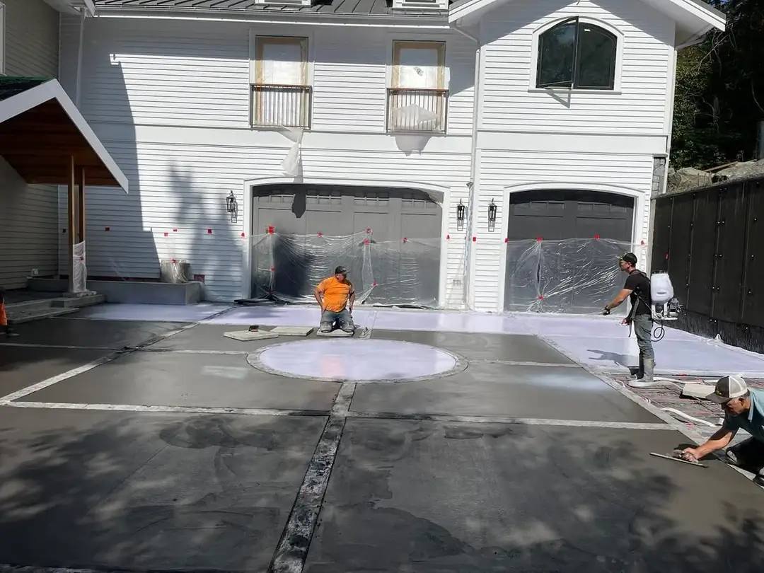 Craftsmen finishing the surface of a large concrete pour with trowels in front of a two-car garage.