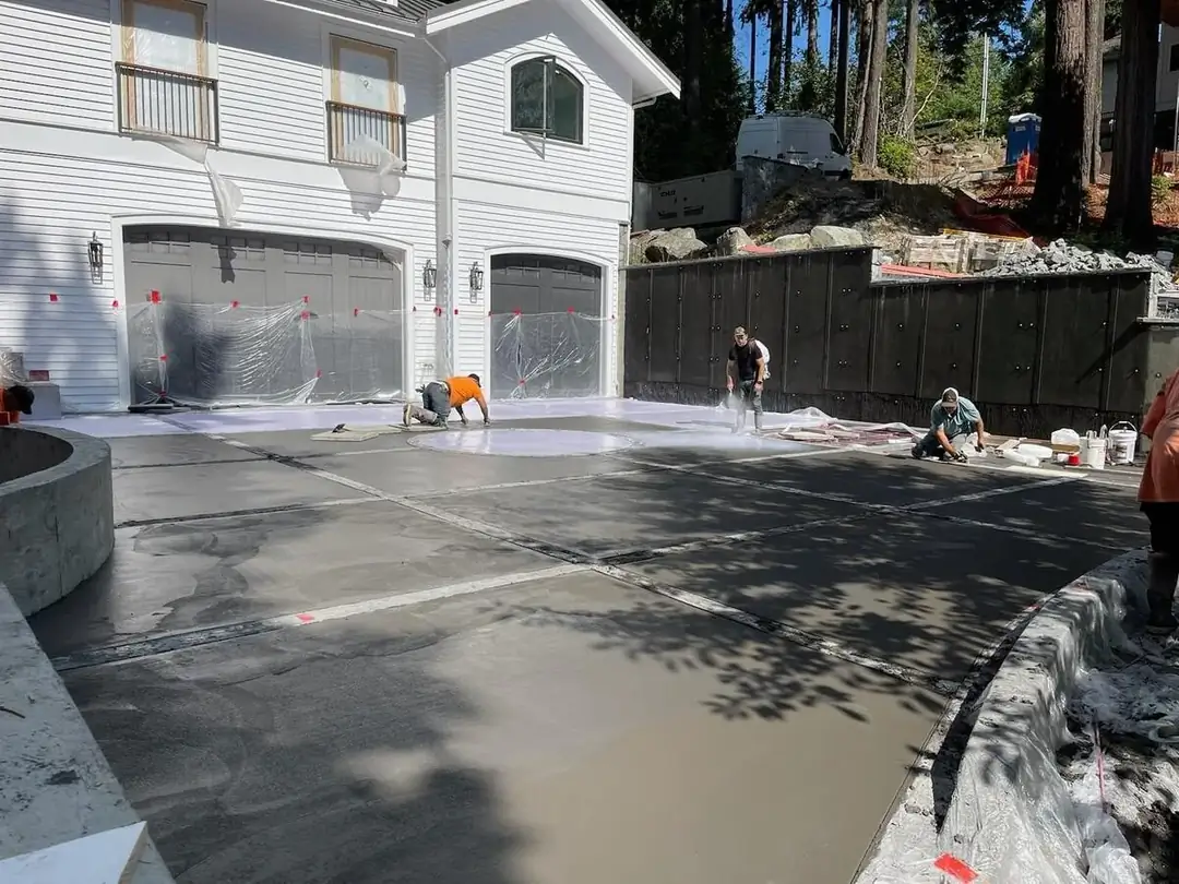 Wide angle view of the concrete driveway installation with multiple workers troweling and finishing the surface.