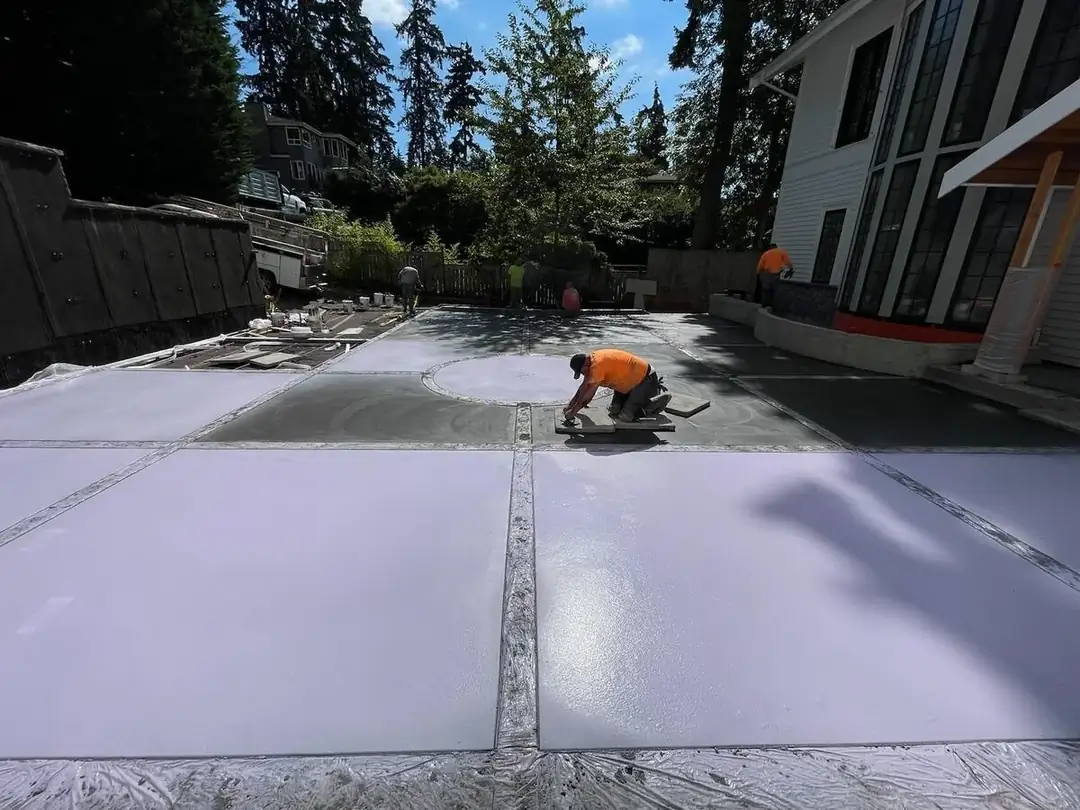 A worker carefully hand-finishing the edges of a concrete pad next to the central circular design element.