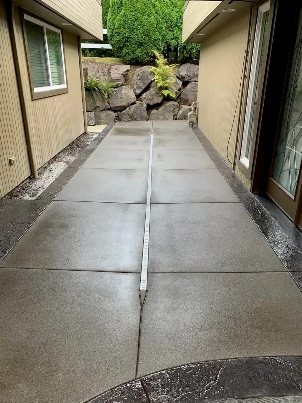 A concrete walkway with a sand finish, saw-cut joints, and a dark stamped border leading to a front door.