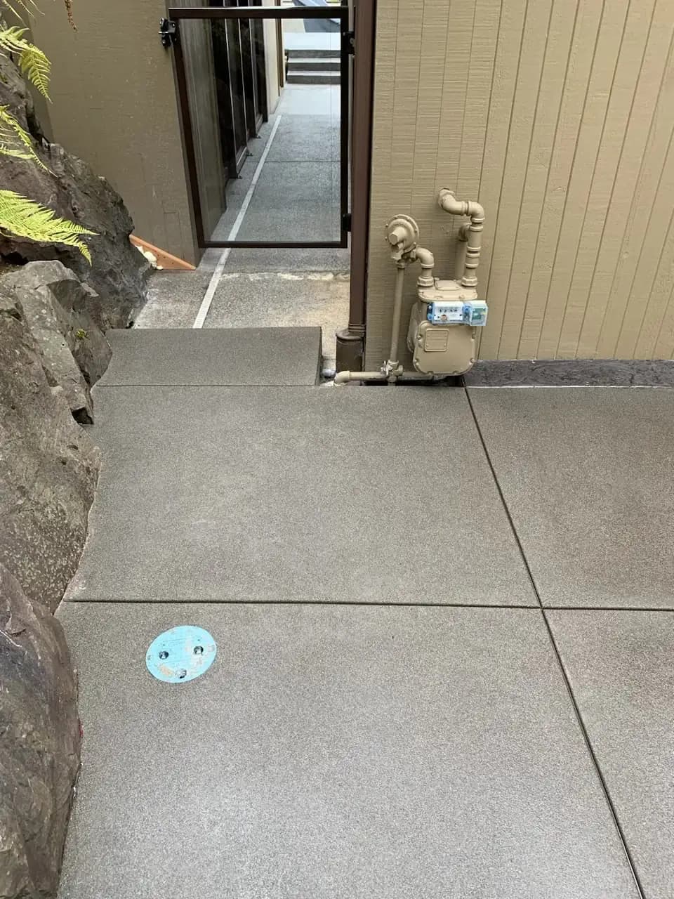Detail of the sand-finish concrete walkway panels adjacent to the home's foundation and rock landscaping.