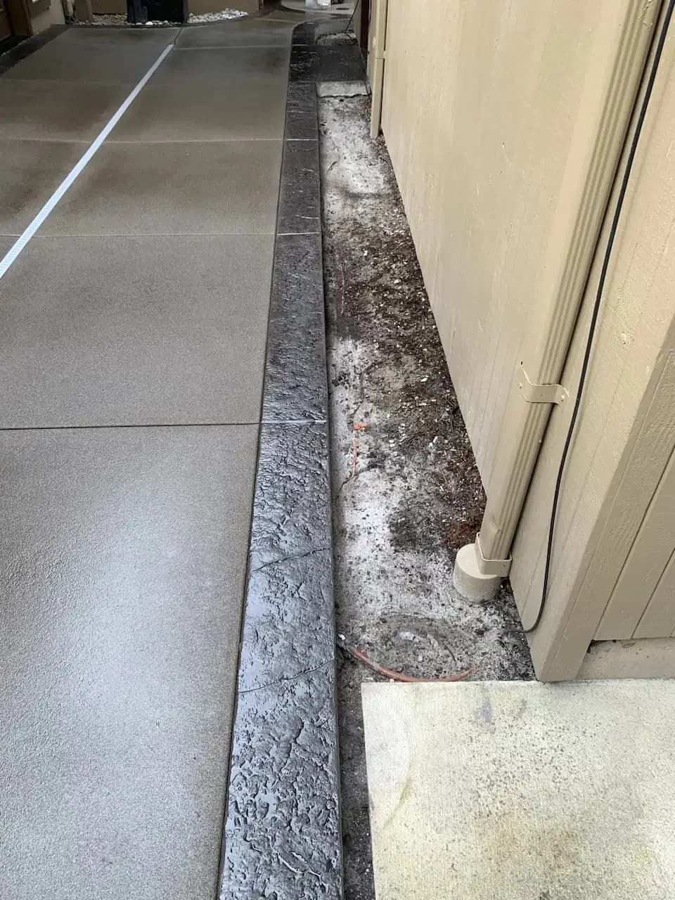 View of the stamped concrete border along the side of the house, separating the walkway from the foundation.