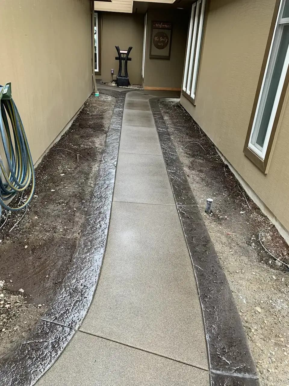 A long concrete walkway with a sand finish and curving stamped borders on both sides leading to a backyard.