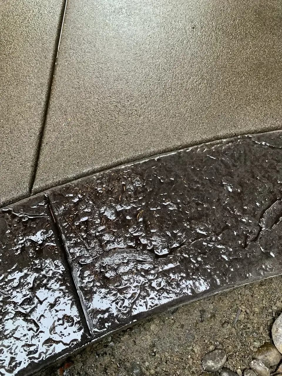 Macro detail shot showing the contrast between the wet, dark stamped concrete border and the sand-finish field.