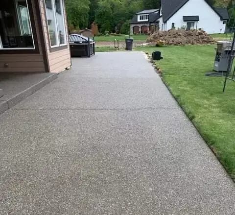 A long exposed aggregate concrete walkway alongside a house in Alderton, WA, with clean saw-cut joints.