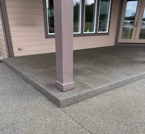 Exposed aggregate concrete patio corner wrapping around a structural support post.