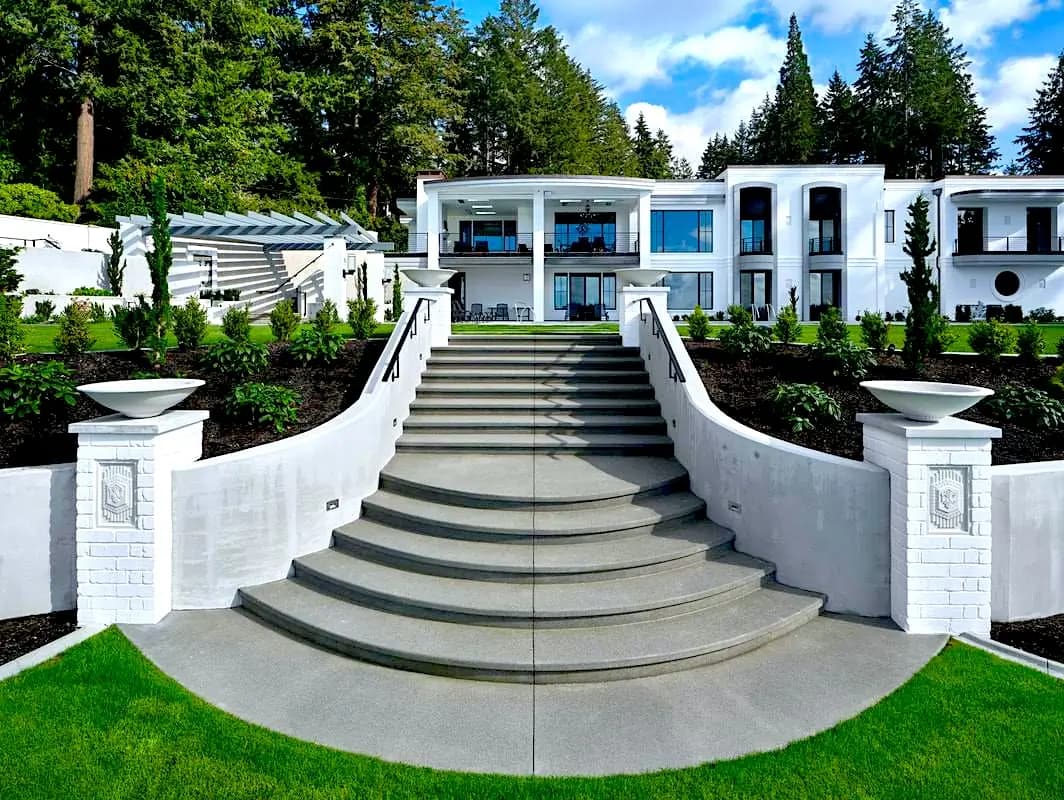 A grand, curved concrete staircase with wide treads and smooth-formed retaining walls leading up to a large home.