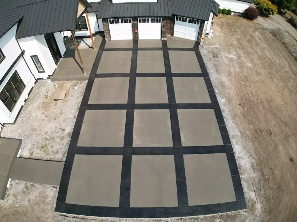 High-angle perspective looking down the concrete driveway towards the three-car garage doors.