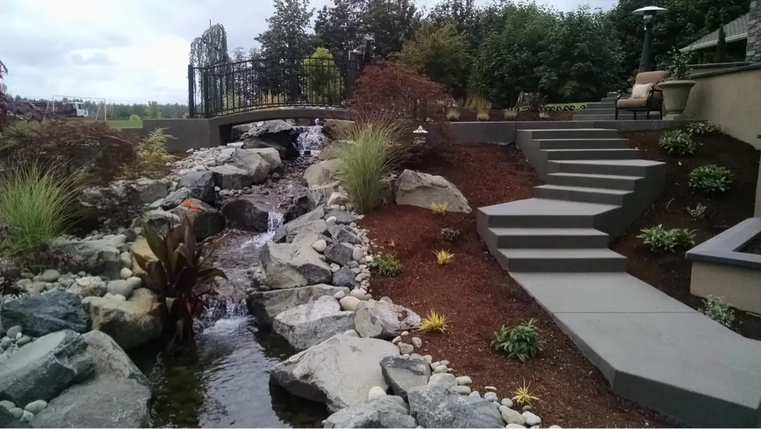 Wide concrete steps and walkway alongside a custom-built stream and water feature in Puyallup, WA.