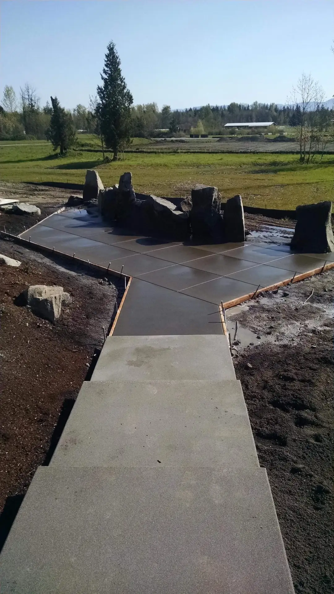 Newly poured concrete walkway and steps with wooden forms still in place around boulders.