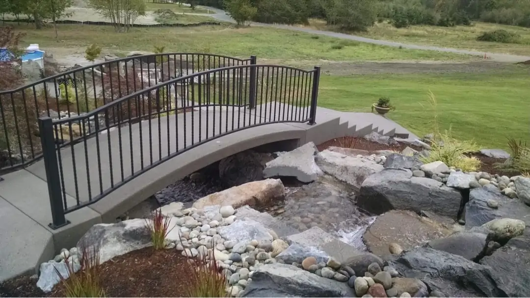 Side profile of the arched concrete bridge, showing its structure over the water feature.