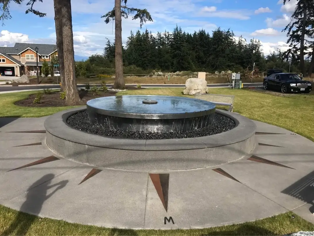 Close-up of the overflowing water from the stainless steel disc onto the dark rocks of the concrete fountain.