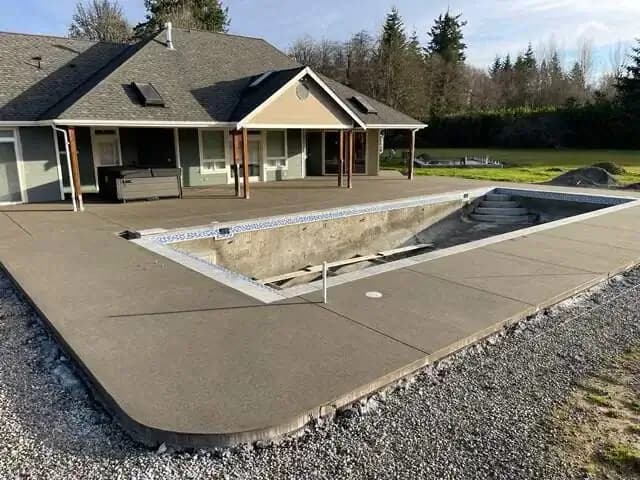 Full perspective of the expansive concrete pool deck surrounding an unfinished pool in Puyallup.