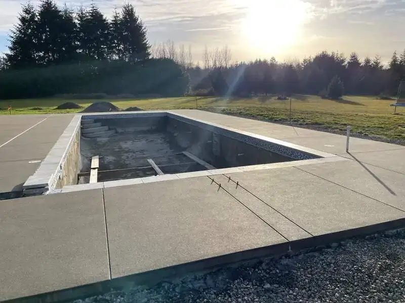 The concrete pool deck shown at sunset, highlighting the clean lines and uniform sand finish of the surface.