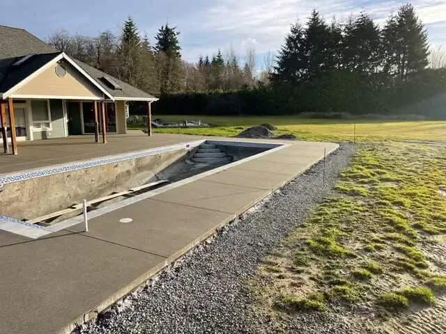 A long view down the side of the pool, showcasing the length of the new concrete walkway and patio area.