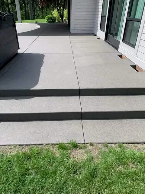 Wide concrete steps with a sand finish leading to a modern patio with saw-cut joints in Auburn, WA.