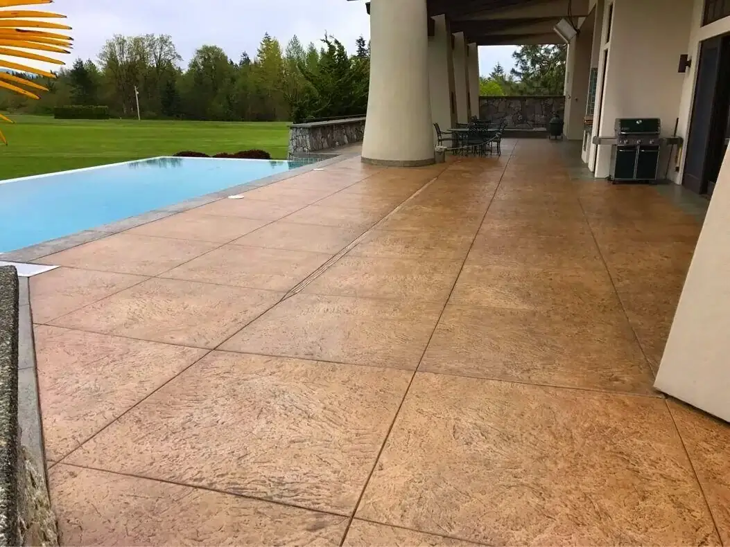 Large-format tile pattern on a stamped concrete patio next to a pool in Bellevue, WA, showing saw-cut joints.
