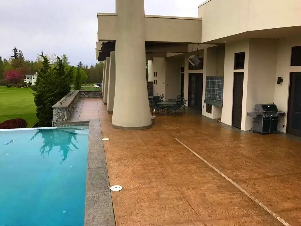 Covered outdoor living area in Bellevue with a sandstone-colored stamped concrete patio and poolside view.